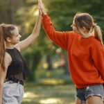 Two women enjoying a sunny day in the park with a joyful high five.