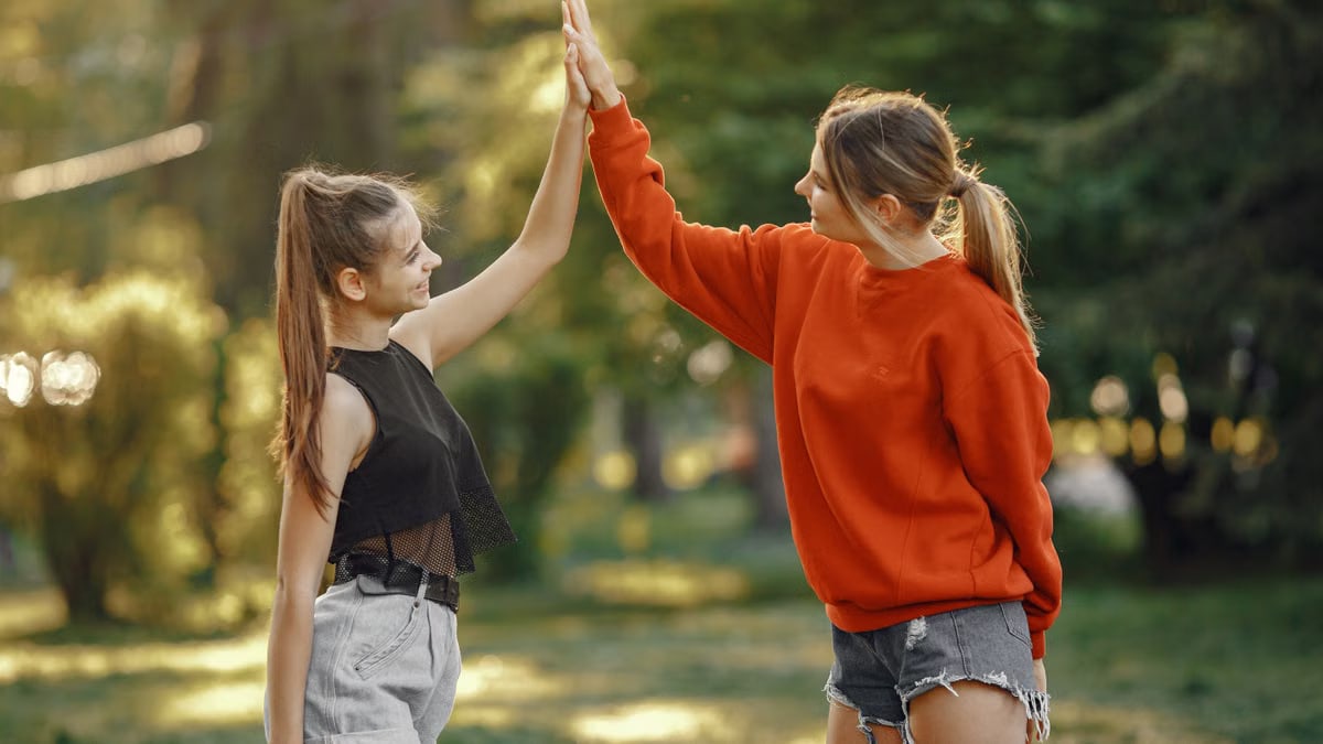Two women enjoying a sunny day in the park with a joyful high five.
